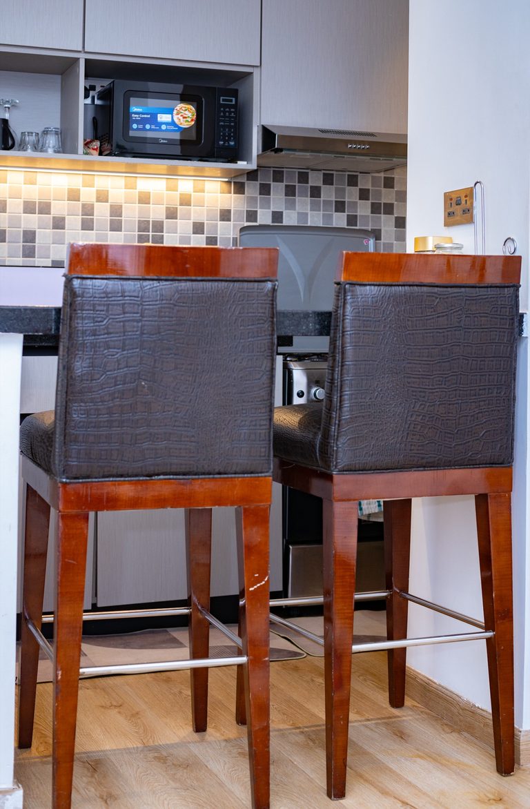Two dark wood bar stools at the kitchen counter, microwave and tiled backsplash behind, The Bloom, Tatu City