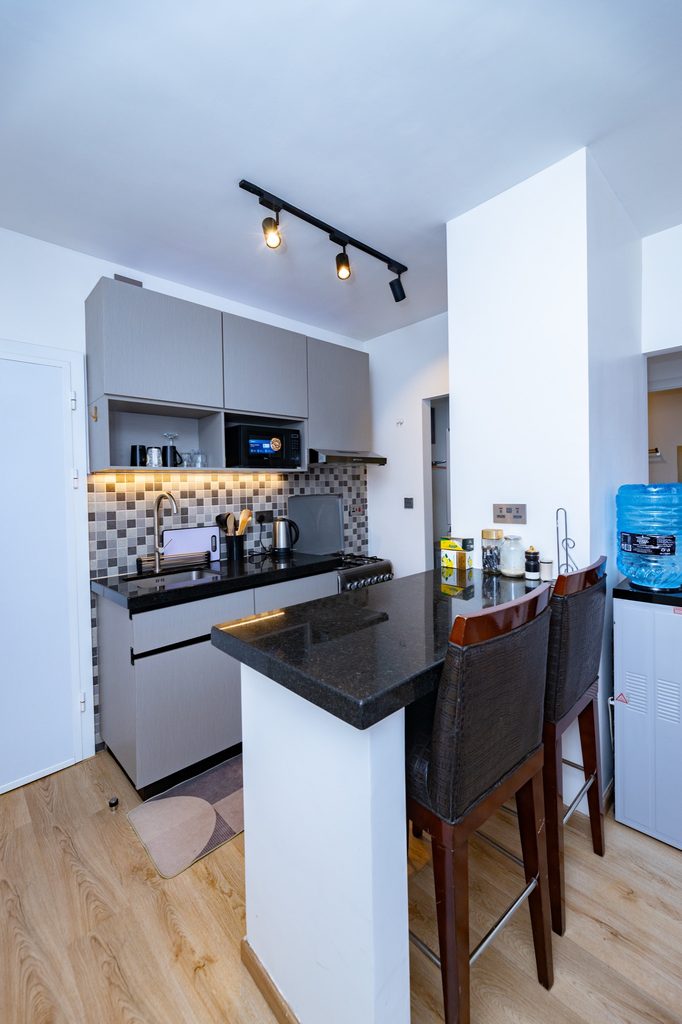 Wide view of the kitchen with a breakfast bar, two wood-framed stools and a water dispenser, The Bloom, Tatu City