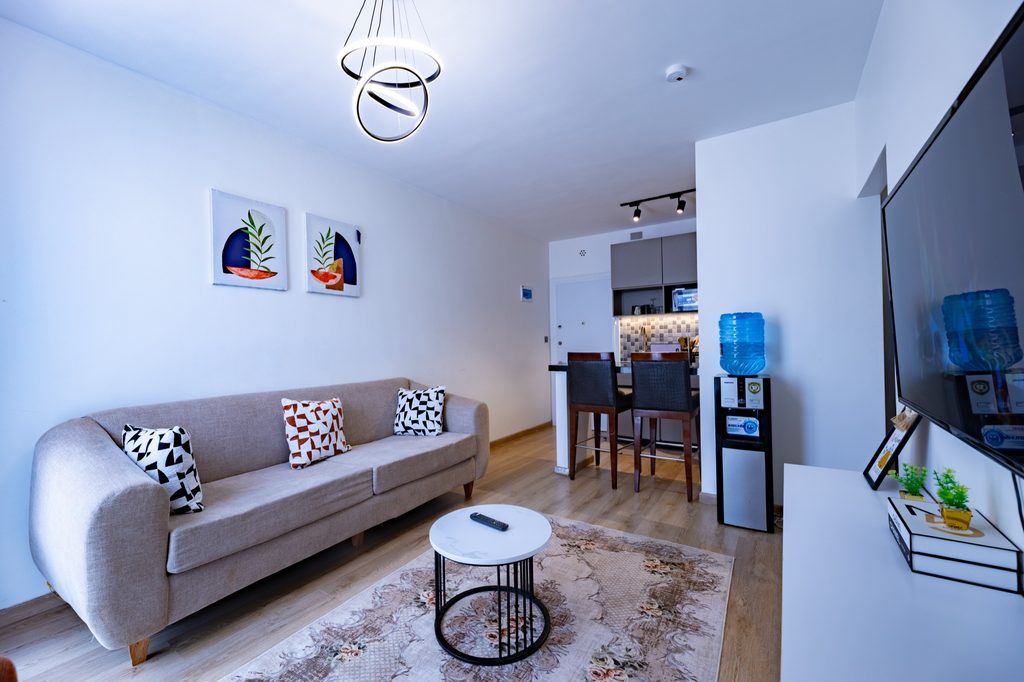 Beige sofa with patterned cushions facing a TV, rust armchair and abstract wall art, The Bloom, Tatu City