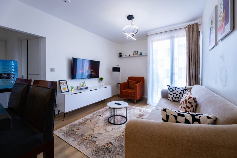 TV wall with a rust velvet armchair and dark dining chairs nearby, The Bloom, Tatu City