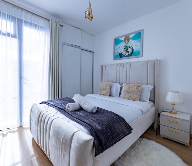 Bed with tufted headboard, purple throw and a bedside lamp on a nightstand, The Canopy, Tatu City