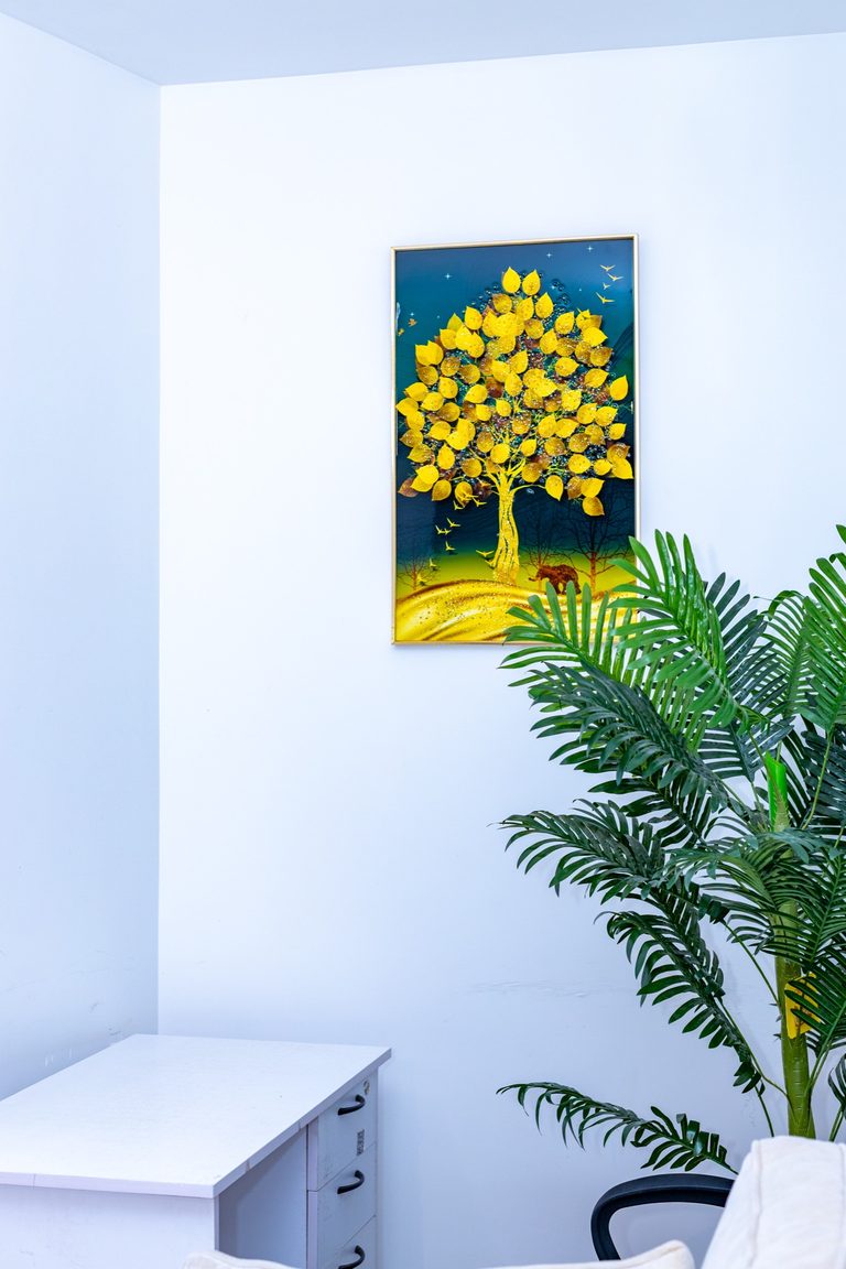 Framed golden tree artwork on the wall beside a plant and desk edge, The Canopy, Tatu City