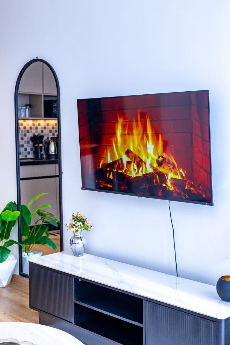 TV showing a fireplace image above a console, mirror and plant beside it, The Canopy, Tatu City
