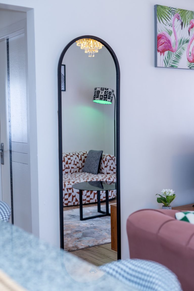 Arched floor mirror in the entryway reflecting the living room sofa and chandelier, The Gallery, Tatu City