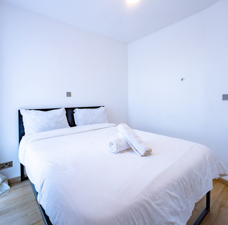 Bed with a dark frame and plain white bedding in a minimally styled bedroom, The Graphite, Tatu City
