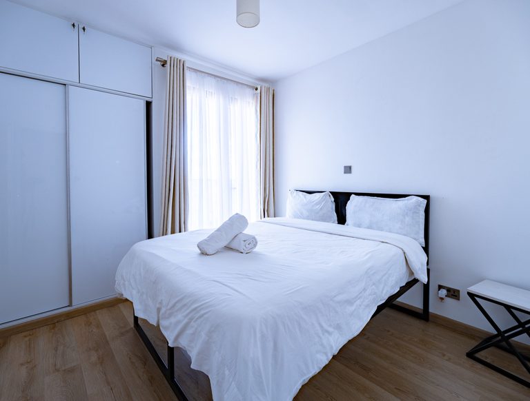 Bed with a dark frame and plain white bedding, rolled towels on top, The Graphite, Tatu City