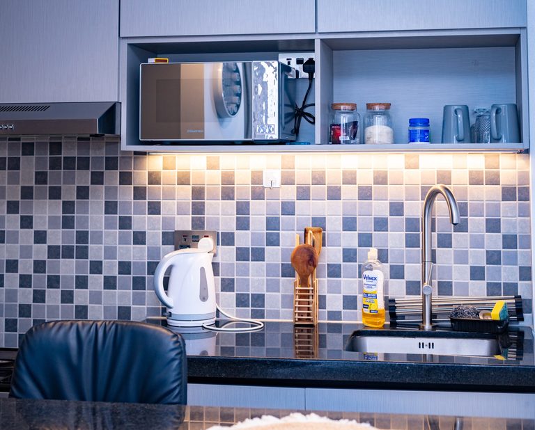 Kitchen shelf with a microwave, jars and mugs above a mosaic tile counter, The Graphite, Tatu City