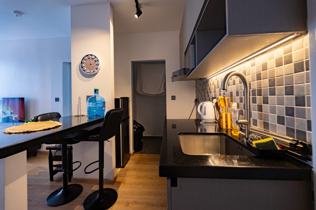 Wide kitchen and living view with a breakfast bar, two stools, wall clock and water dispenser, The Graphite, Tatu City