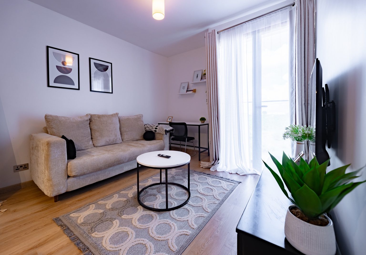 Sofa with cushions facing a desk and chair, curtained balcony door letting in daylight, The Graphite, Tatu City