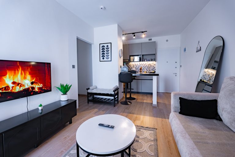 TV wall playing a fireplace video, black media console, wall clock and the kitchen bar beyond, The Graphite, Tatu City