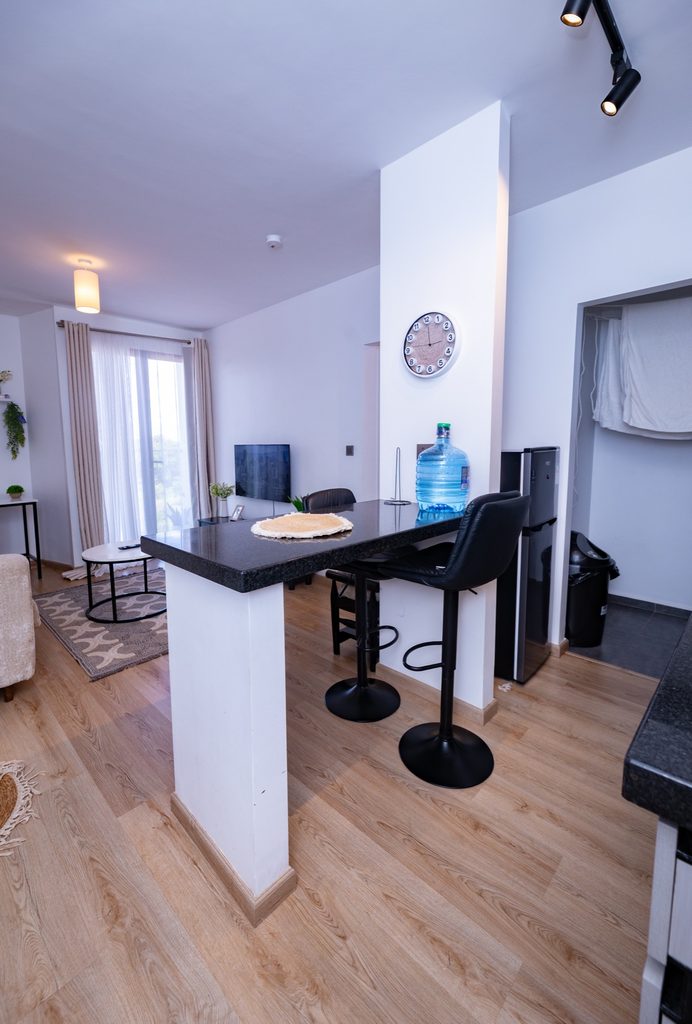 Wide view of the living room sofa, dining bar and open kitchen with a wall clock and water dispenser, The Graphite, Tatu City