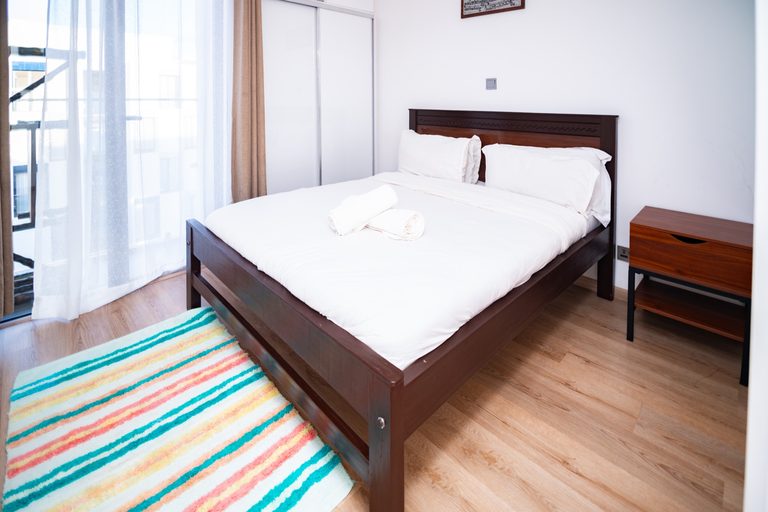 Dark wood bed frame with striped rug, second wide view, The Hearth, Tatu City