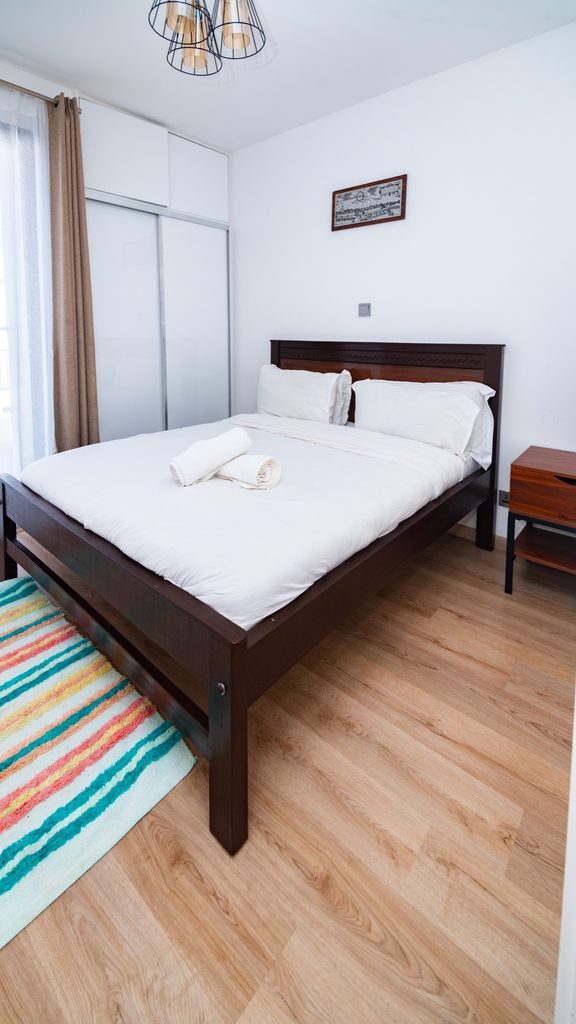 Dark wood bed frame with a colourful striped rug, wide view, The Hearth, Tatu City