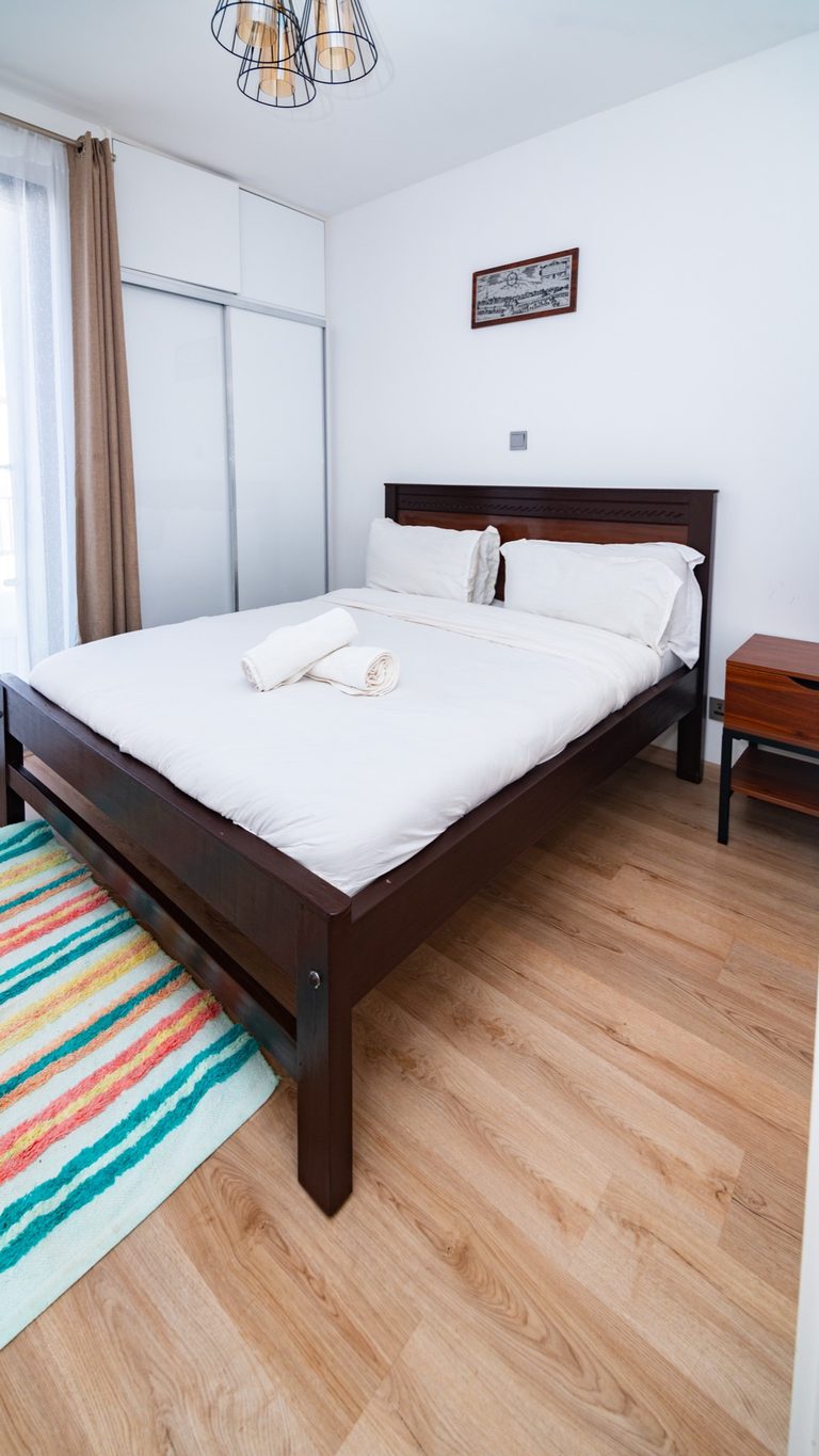Dark wood bed frame with a colourful striped rug, wide view, The Hearth, Tatu City