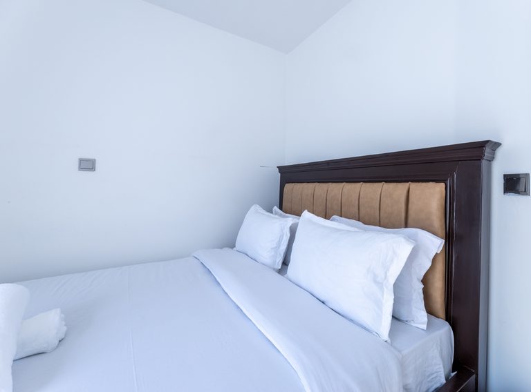 Bed with dark wood frame, tan headboard and crisp white bedding, The Metro, Tatu City