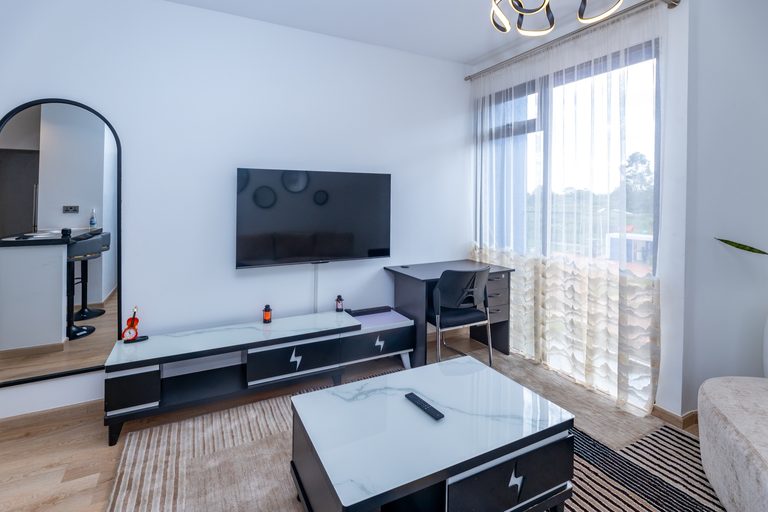 Living room with TV and desk, tall window showing greenery outside, The Metro, Tatu City