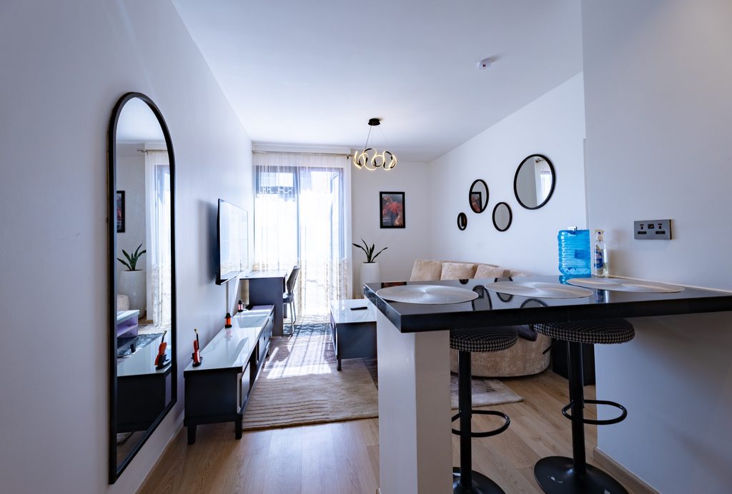 Living room with tall arched mirror, wall mounted TV, sofa and sheer curtained balcony door, The Metro, Tatu City