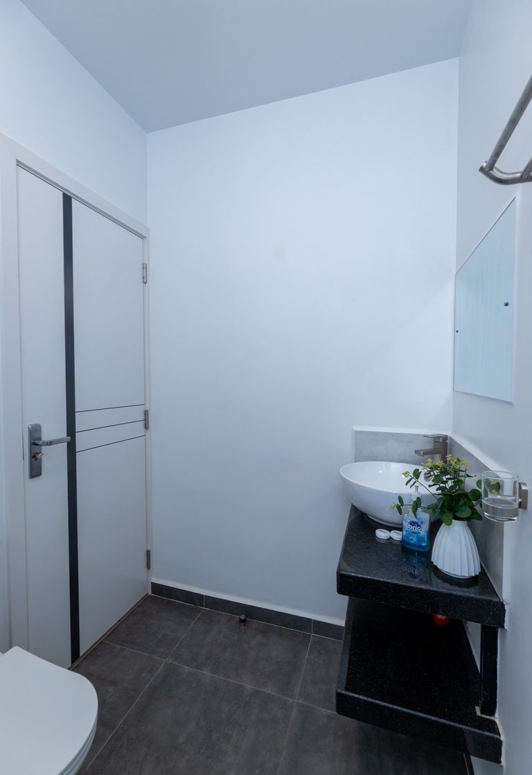Bathroom with a toilet, a sliding door and a small sink stand with flowers, The Tide, Tatu City