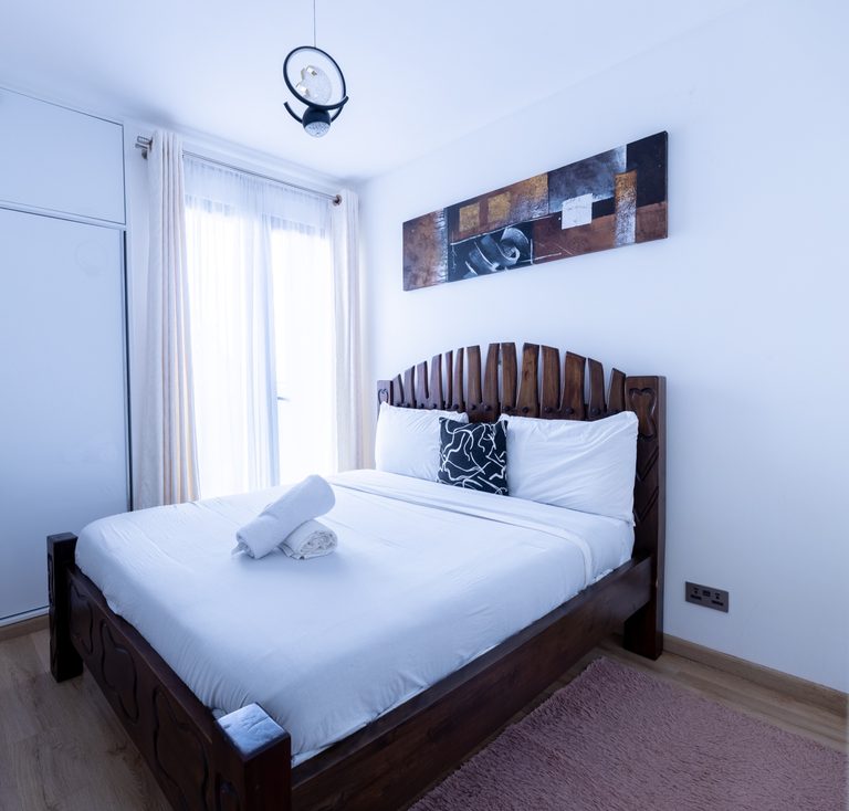 Bed with a carved wood headboard, white bedding and a brown abstract wall painting, The Tide, Tatu City