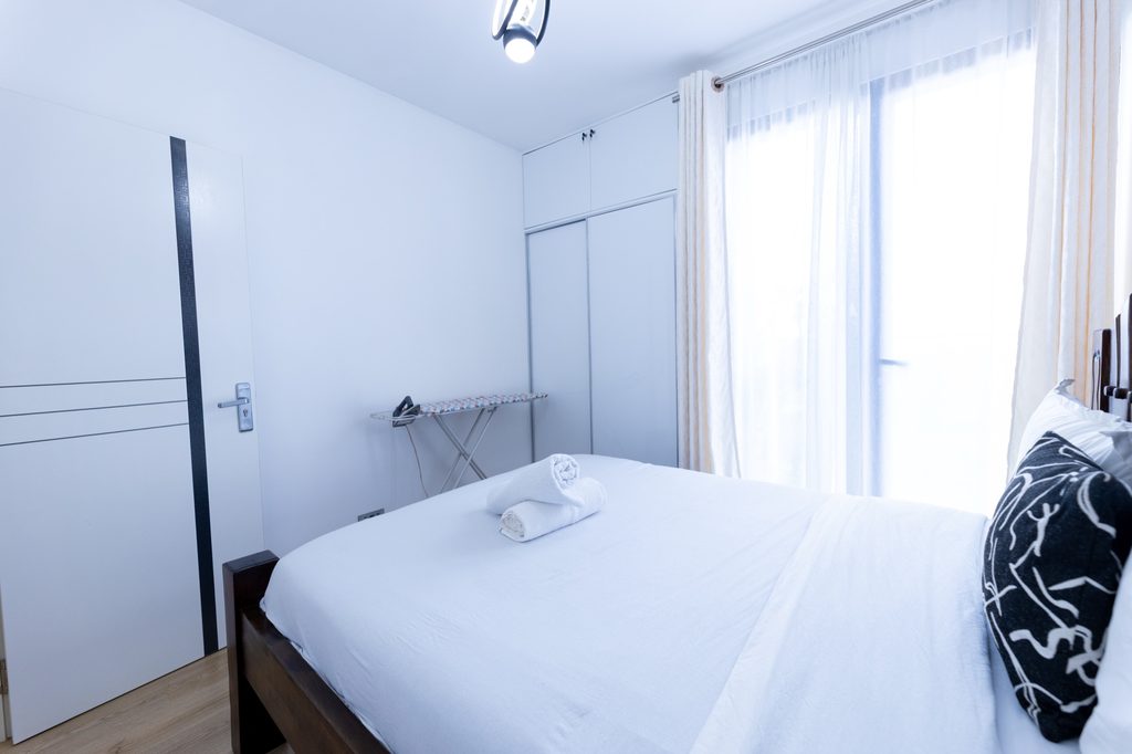 Bed with a wood slatted headboard and a patterned pillow, sliding wardrobe and curtained window, The Tide, Tatu City