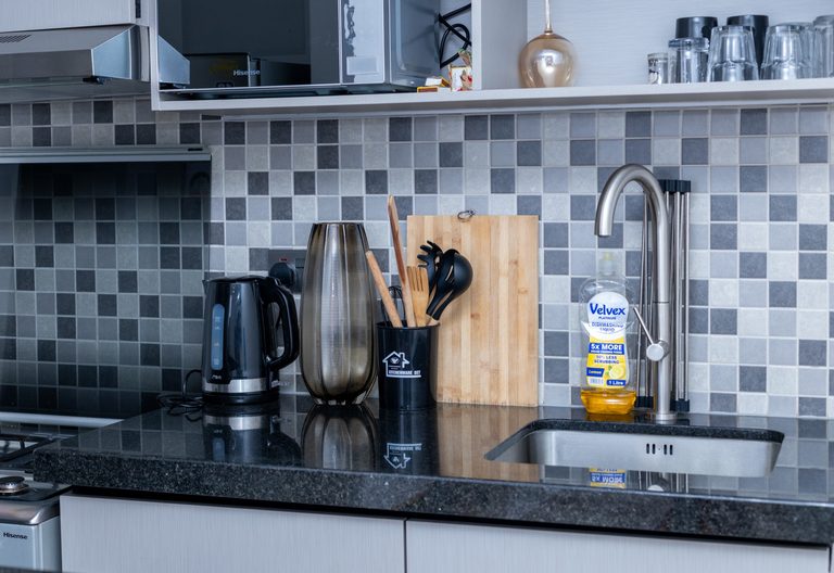 Kitchen counter with a kettle, a vase of utensils, a cutting board and the sink, The Tide, Tatu City