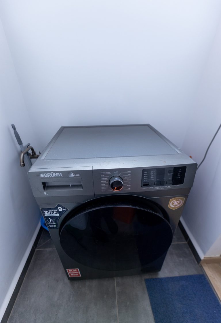 Front-load washing machine standing in a small tiled laundry nook, The Tide, Tatu City