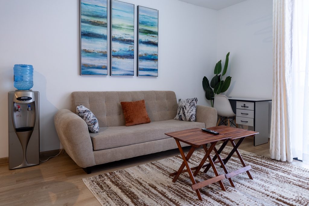 Beige sofa with rust and patterned cushions below a blue abstract triptych, with a desk in the corner, The Tide, Tatu City