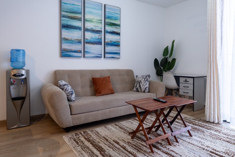 Beige sofa with rust and patterned cushions below a blue abstract triptych, with a desk in the corner, The Tide, Tatu City