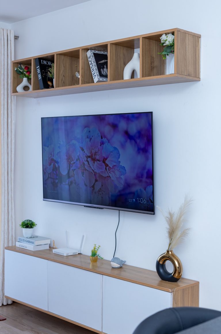 TV wall with a wooden shelf of books and vases, seen from the seating area, The Tide, Tatu City