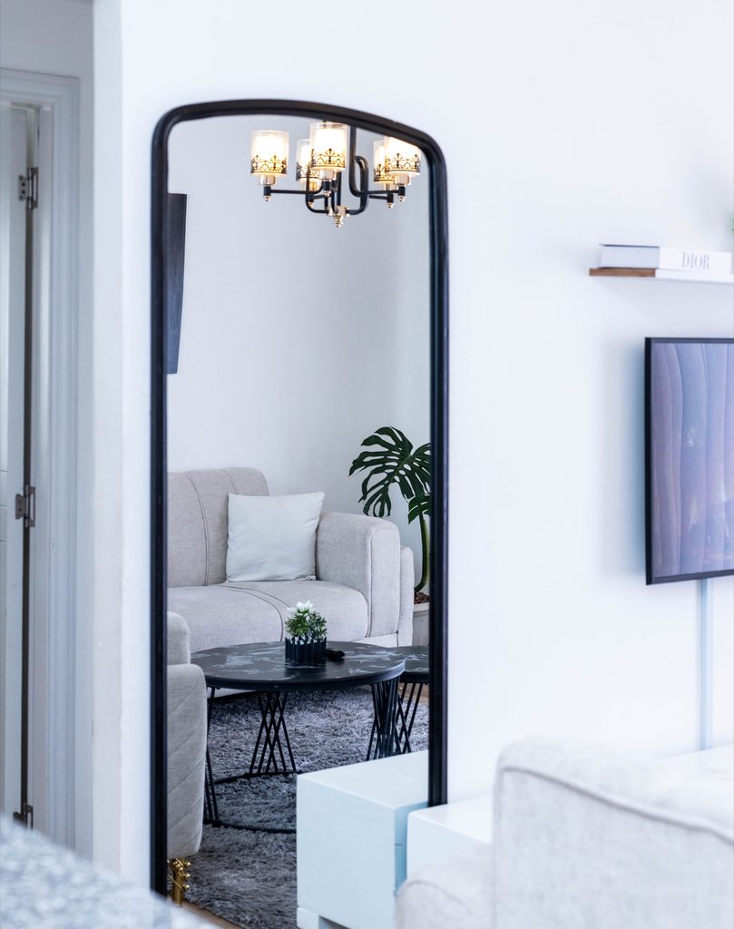 Cream sofa and TV console with an arched black frame floor mirror in the living room, The Velvet, Tatu City